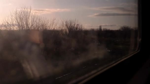 Der Blick aus dem Zugfenster auf die vorbeiziehende Landschaft. der Himmel bei Sonnenuntergang. — Stockvideo