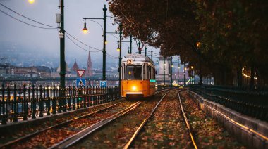 Sarı bir tramvay Tuna nehri kıyısında 2 numaralı yolda ilerliyor. Budapeşte 'de bulutlu bir sonbahar akşamı.
