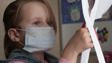 Karantina, koronavirüs tehdidi. Tıbbi maskeli bir çocuk masaya oturur ve kağıt keser. Karantina ödevi.