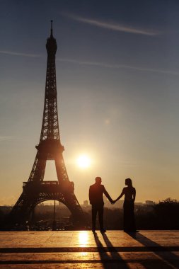 Eyfel Kulesi 'nin arka planında yeni evlilerin silueti var. Çift el ele tutuşuyor ve birbirlerine bakıyor. Paris 'te şafak.