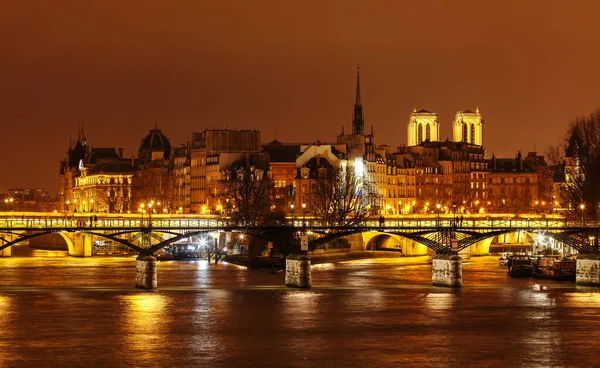 Ponte das Artes no fundo da ilha de Cite à noite. Notre Damm é visto por trás dos telhados dos bairros da ilha de Cite . — Fotografia de Stock