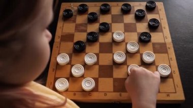 Küçük bir kız kendi kendine dama oynuyor. Bir çocuk evde masa oyunu oynuyor.