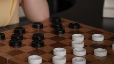 Küçük bir kız kendi kendine dama oynuyor. Bir çocuk evde masa oyunu oynuyor.