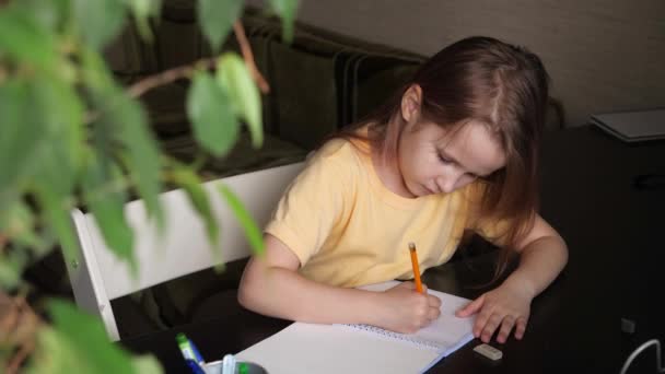 En liten flicka sitter vid ett bord och ritar på papper. — Stockvideo