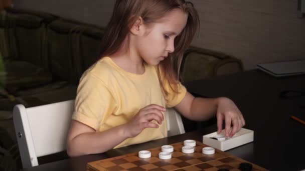 En liten flicka sätter pjäser på tavlan. Ett barn leker brädspel hemma. — Stockvideo
