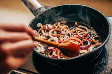 Soğanlar tavada kızarır. Kadın eli soğanı karıştırır..