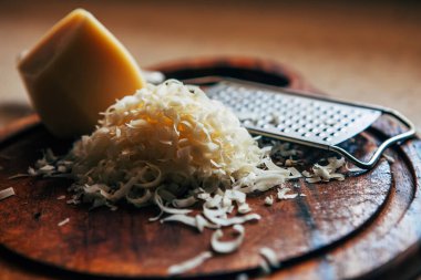 Kesme tahtasında rendelenmiş peynir. Bir parça peynir ve rendenin yanında..