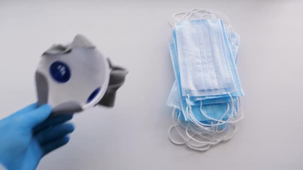 Läkarens hand sätter en respirator på ett bord bredvid medicinska masker — Stockvideo