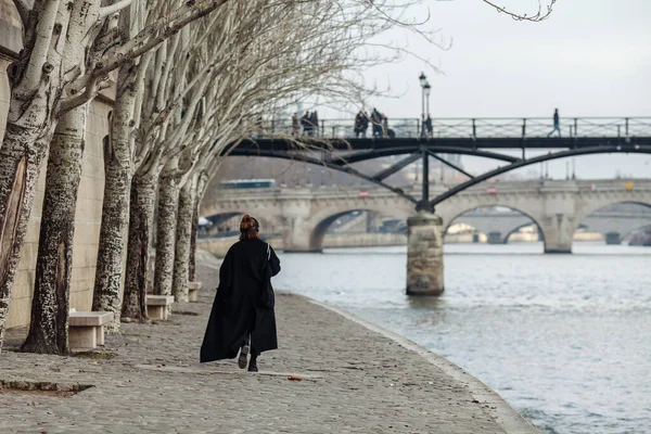 Een vrouw in een zwarte jas loopt langs de Seine.. — Stockfoto