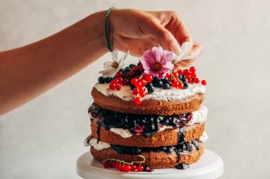 Dişi bir el taze çiçeklerle bir çilekli pasta süslüyor..