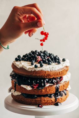 Bir kadın eli pastayı taze böğürtlenlerle süslüyor.