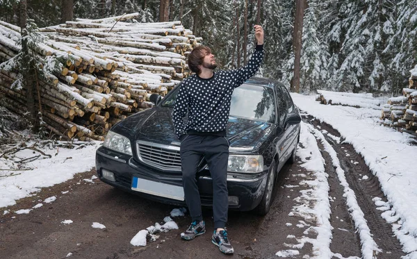 Homem fazendo selfie no telefone perto de carro na floresta de inverno — Fotografia de Stock