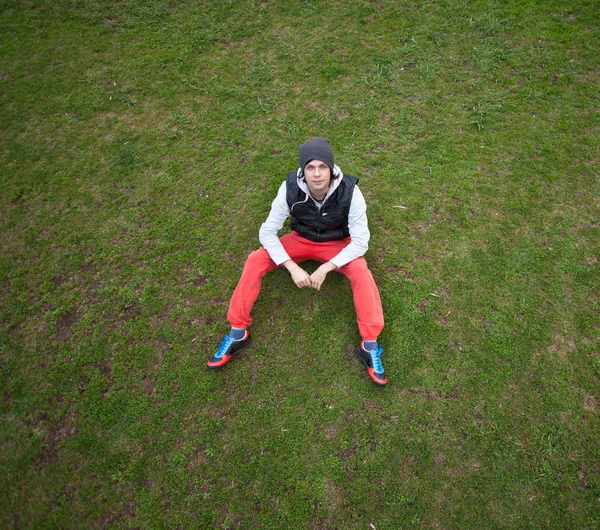 Sonbaharın kırmızı pantolon ile çimlerde oturan adam