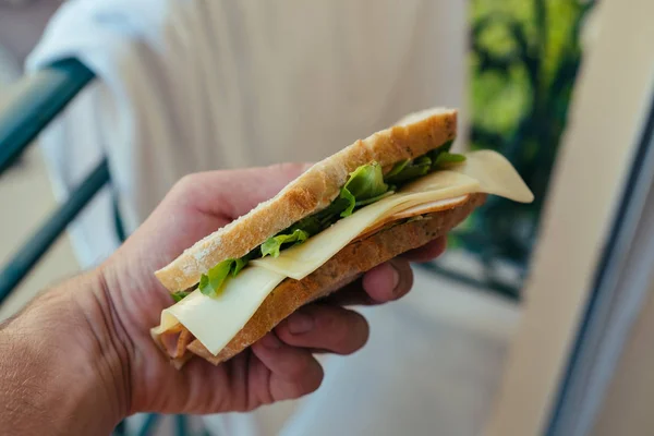 Sanduíche de pão branco com zumbido e salada na mão dos homens em Mônaco — Fotografia de Stock