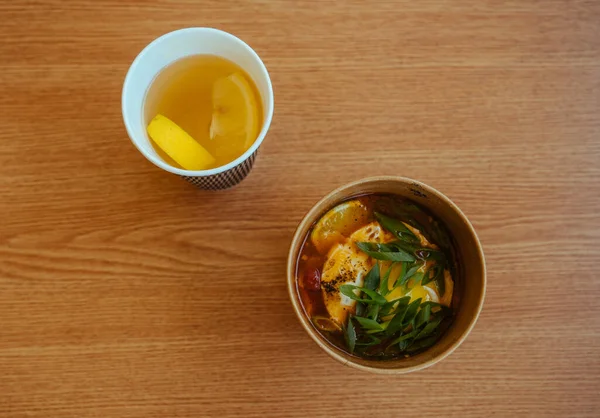 Asian soup in a paper cup with lemon Tea on wooden table