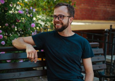 Siyah tişörtlü bir adam, sakallı bir gözlüklü yaz şehrinde bankta.