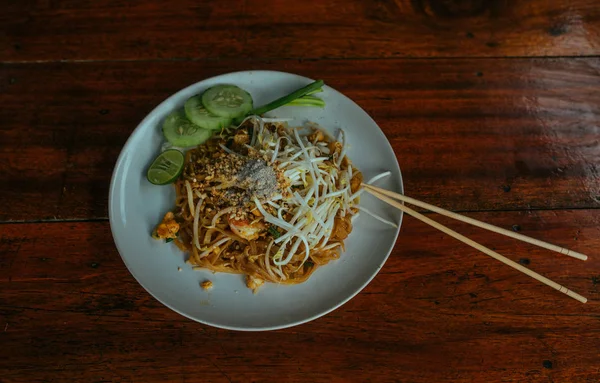 Almohadilla de fideos tailandeses con pollo y pepinos y palos de bambú en la mesa de madera — Foto de Stock