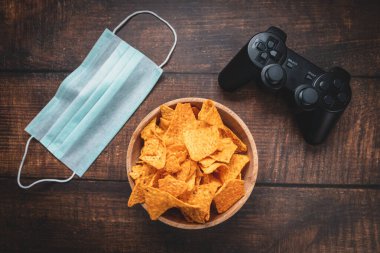 Oyun konsolu RC, bir kase cips ve ahşap masada tıbbi maske. Coronavirus Covid-19 karantinaya alınmıştır..