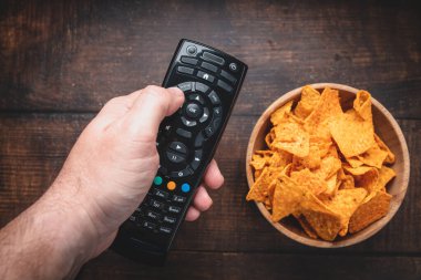 Televizyonun uzaktan kumandasının yanındaki tahta kasede yanmış ahşap arka planda çipler var. Üst Manzara. Kapatın. Ayarlanmış.