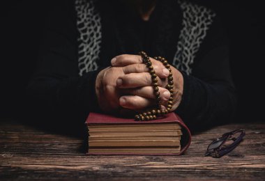 Elleri kapalı yaşlı kadın kutsal kitapta tespihi tutuyor evde kalıyor ve korunmak için dua ediyor. Yaşlılık koronavirüsü covid-19 pandemi kavramı..