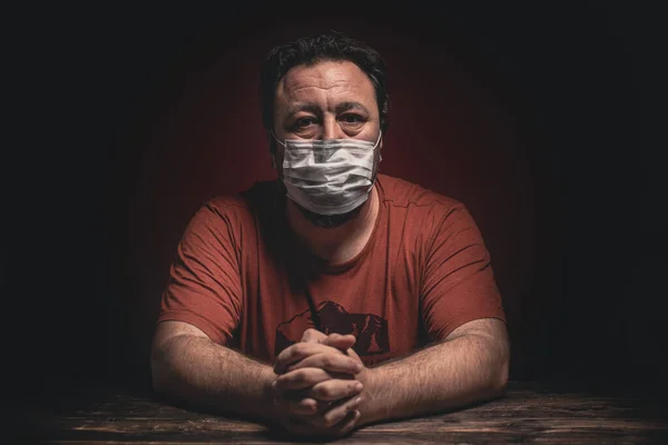 Attractive man with protective medical mask sitting desperate on the table looking worried, depressed, thoughtful and lonely suffering depression because of Covid-19 Coronavirus quarantine.