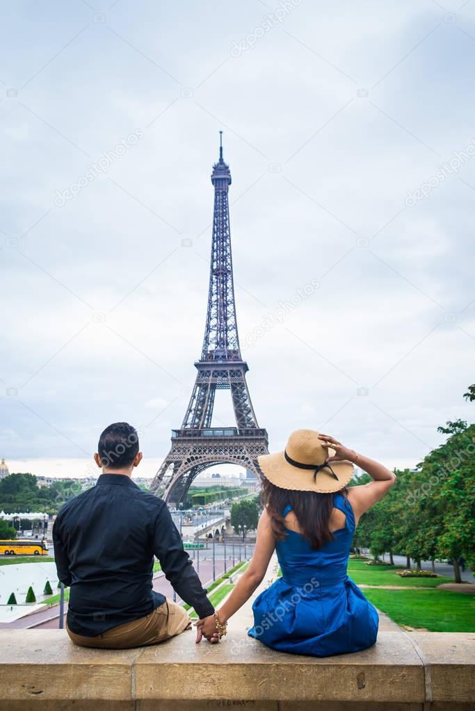 Young couple of tourists sitting in front of Eiffel tower in Paris