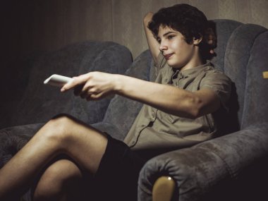 genç çocuk içinde kanepede oturan uzaktan kumanda ile tv izliyor