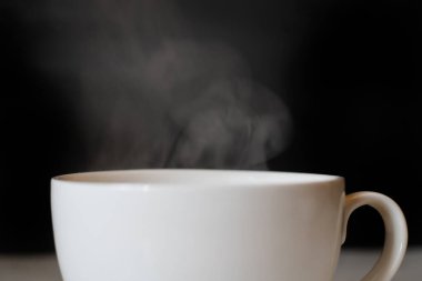 Siyah arka planda kahve içilen beyaz bardaktan sıcak buhar.