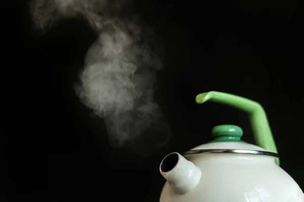 the kettle with hot boiling water and the steam comes out from it on dark backgrounds