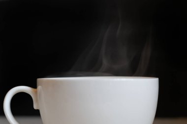 Siyah arka planda kahve içilen beyaz bardaktan sıcak buhar.