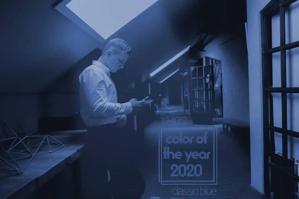 Fiatal irodai dolgozó használja okostelefonját, színe a 2020-as év trend, klasszikus kék tónus — Stock Fotó