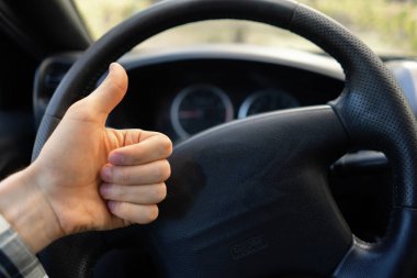 first person view of driver showing thumb up in front of steering wheel clipart
