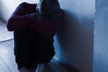 Depresyonda olan mutsuz bir adam koridorda yerde oturuyor.