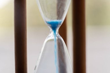 Eski bir kum saatine dökülen mavi kumların makro görüntüsü.