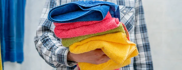 Человек в прачечной держит стопку чистых полотенец цвета — стоковое фото