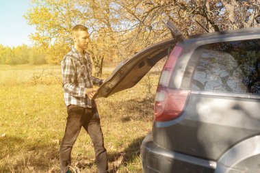 Ormandaki bir erkek turist bagajı açar ve içeri bir şeyler sokar.