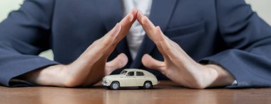 Adam elleri masadaki küçük araba modelini, sigorta konseptini kapsıyor.