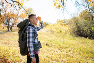 Genç erkek turist güneşli ormanda sırt çantasıyla geziyor, vahşi bir yürüyüş yapıyor.