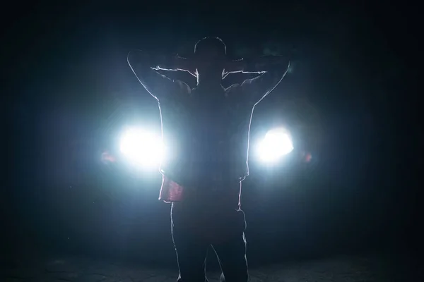 silhouette of a male criminal suspect with hands up during night pursuit in front of the police car headlights