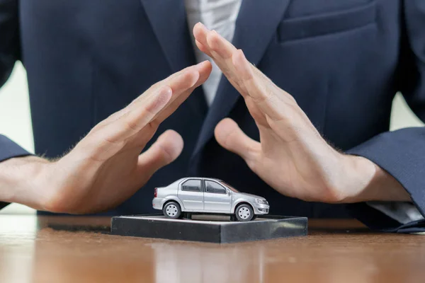 the man hands cover the little car model on the table, the insurance concept