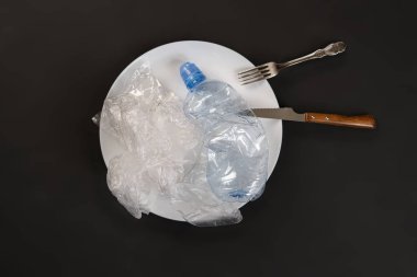 Beyaz tabak, bıçak ve çataldaki plastik atıkların üst görünümü, çevreyi sorunlardan korur