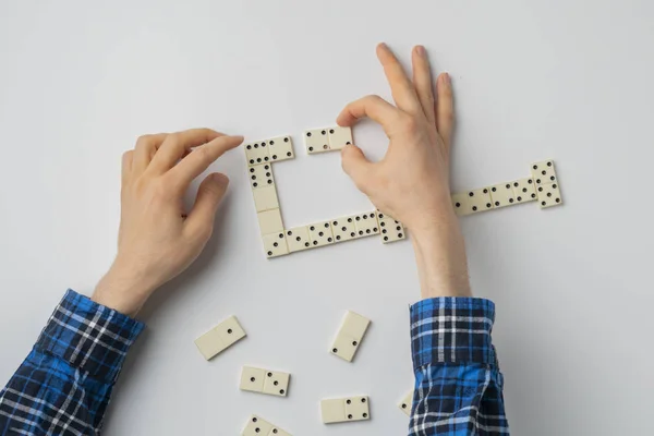 Una mano cercana de la persona sosteniendo piezas dominó y jugar el juego en la mesa blanca — Foto de Stock