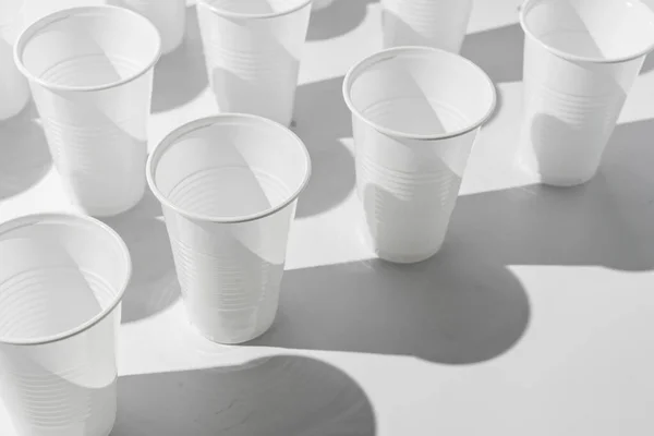Абстрактный рисунок пластиковых чашек на цветной поверхности с резкими модными тенями — стоковое фото