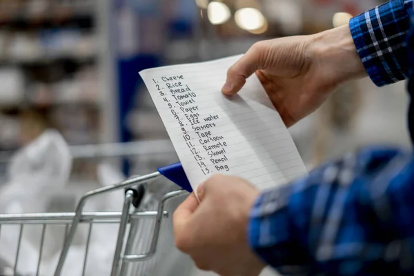Руки человека, держащего лист со списком покупок и проверяющего покупку продуктов в продуктовом магазине — стоковое фото