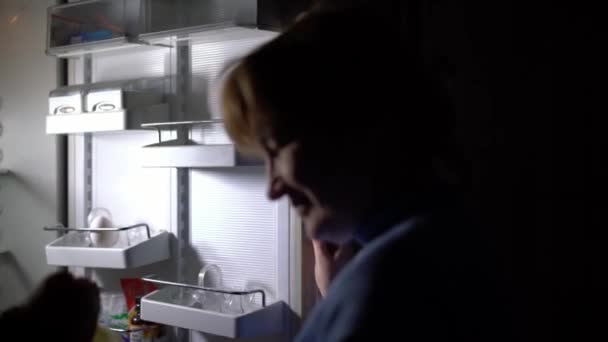Женщина у открытого холодильника ночью — стоковое видео