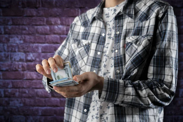 person standing against the color wall and counting the bunch of money cash