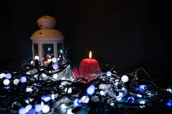 Uma vela vermelha com luzes de Natal na luz atmosférica — Fotografia de Stock