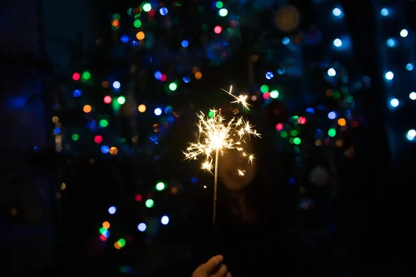 小女孩在一棵圣诞树的背景下拿着烟火的火 — 图库照片