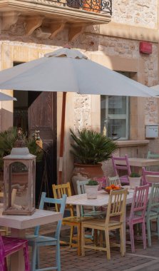 Evin önündeki şemsiyenin altında çok renkli sandalyeler olan bir masa.
