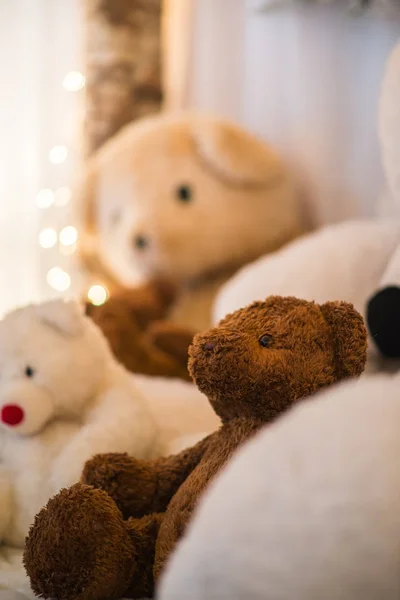 茶色のテディベアは 背景にクリスマスライトと白 Stuffted クマの腕の中に産む コージーホリデイズ — ストック写真